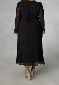 Musta, pitkähihainen mekko, jossa on läpinäkyvää kangasta, joka on koristeltu tähtikuosisilla. Joustava vyötärö, leveät hihat ja polveen saakka ylettyvä pituus. Hopeiset paljettikengät.