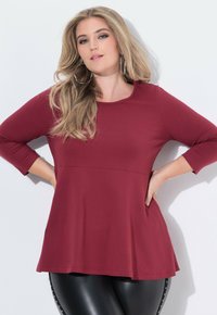Bordeauxfarbene Langarm-Bluse mit Rundhalsausschnitt, lockerem Schnitt und ausgestellt geschnittenem Saum, kombiniert mit schwarzen Leggings mit Nietenakzenten.