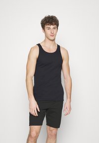 Schwarzes Baumwoll-Top mit rundem Ausschnitt, ärmellosem Design und schmaler Passform, kombiniert mit schwarzen Shorts. Glatte Textur und minimalistische Details.