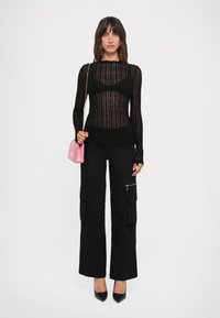 Top sheer nero a maniche lunghe con motivo testurizzato, abbinato a pantaloni cargo neri con tasche laterali e décolleté neri a punta. Borsa rosa.