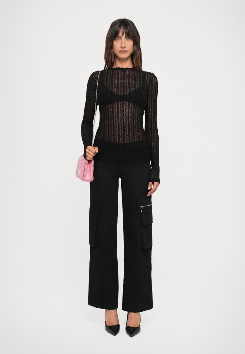 Top sheer nero a maniche lunghe con motivo testurizzato, abbinato a pantaloni cargo neri con tasche laterali e décolleté neri a punta. Borsa rosa.