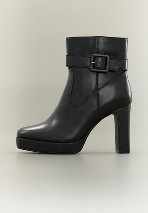 Bottine noire en cuir avec talon haut carré et sangle décorative à boucle autour de la partie supérieure de la cheville.