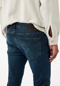 Denimjeans i mörkblått med en mjuk textur. Har två bakfickor och en brun läderpatch på midjeband. Styla med en ljusfärgad blus.