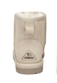 Beige suede ankle boots with soft lining, featuring a rear pull tab and a branded logo on the heel. Minimalist design with a simple tread.