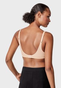Sostenedor beige con un acabado suave, tirantes anchos y un diseño de espalda baja. Cuenta con tirantes ajustables y un cierre de gancho y ojo.