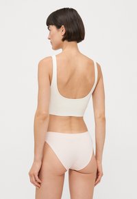 Hvit crop topp med scoop rygg og brede stropper, kombinert med lyserosa mid-rise truser. Glatt tekstur uten synlig utstyr eller mønstre.