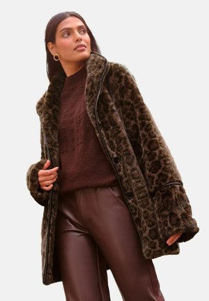 Faux-Fur-Leopardmuster-Mantel mit Schalkragen, schwarzer Paspel und großen Knöpfen, getragen über einem braunen strukturierten Pullover und braunen Lederhosen.