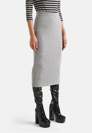 Femme portant une jupe midi côtelée grise, des bottes plateformes à hauteur de genou en cuir verni noir, et un haut à manches longues rayé noir et blanc.