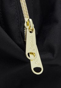 Sac en tissu noir avec une fermeture éclair dorée. La fermeture éclair comporte deux tirettes, affichant la marque "anello" et une finition lisse et texturée.