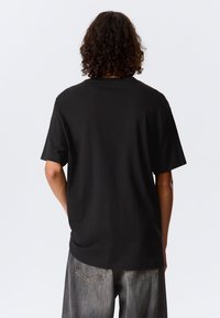 Čierne tričko s krátkym rukávom a okrúhlym výstrihom. Vyrobené z hladkej tkaniny, má voľný strih a ploché švy, nosené s šedými džínsami.