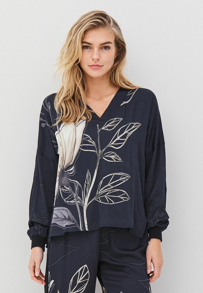 Marineblauwe blouse met lange mouwen en een V-hals, versierd met een groot bloemen- en bladraster in crème- en gouddtinten; ontspannen pasvorm en textuurstof.
