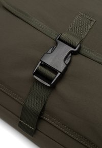 Sac de couleur vert olive foncé avec une texture lisse, comportant une boucle en plastique noir et une bandoulière verte réglable. Coutures visibles le long des bords.