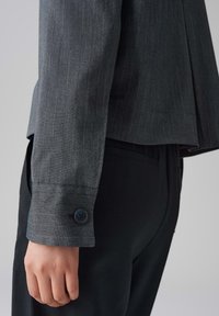 Grijze gestreepte stoffen shirt met een getailleerde pasvorm, voorzien van een knoopmanchet en een lichte plooi aan de achterkant, gecombineerd met zwarte broek.