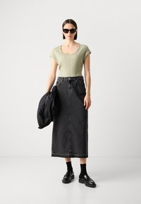 Vihreä ribattu lyhythihainen paita, korkeavyötäröinen musta farkkuhame, mustat kengät ja aurinkolasit, pitää mustaa takkia, minimalistic design.