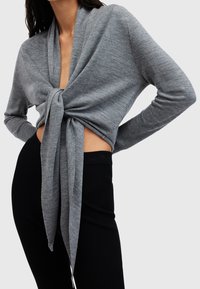 Jasnoszary dzianinowy krótki top z kopertowym fasonem i detalem z supełkiem z przodu, z długimi rękawami i prążkowanym wykończeniem, zestawiony z czarnymi dopasowanymi spodniami.