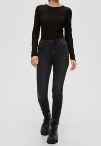 Svart långärmad topp med ribbad textur, kombinerad med mörk tvättade skinny jeans med hög midja, två framfickor och svarta snörkängor.