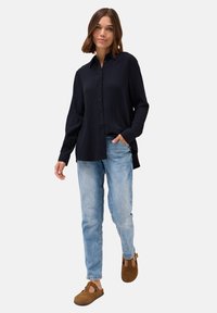 Marineblaues Hemd mit Knöpfen, aus strukturiertem Stoff, mit langen Ärmeln und lockerer Passform, kombiniert mit hellblauen Jeans und braunen Holzclogs.