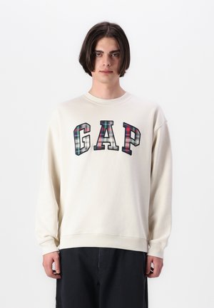 Krémová mikina s kulatým výstřihem a dlouhými rukávy. Má logo "GAP" v kostkovaném vzoru. Měkká textura a volný střih.
