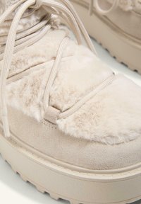 Beżowe sneakersy na platformie z zamszowym wierzchem o puszystej teksturze, elastycznymi sznurówkami i solidną gumową podeszwą. Zauważalne detale w szyciu.