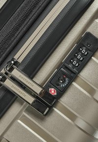 Valise rigide de couleur or métallisé avec une surface texturée, double fermeture éclair argentée et un verrou à combinaison approuvé par la TSA.