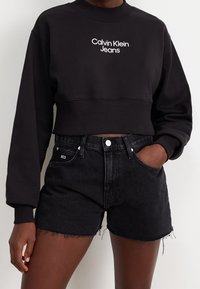 Svart kort sweatshirt med vitt "Calvin Klein Jeans"-logotyp. Matchad med svarta denimshorts med trasig kant och framfickor.