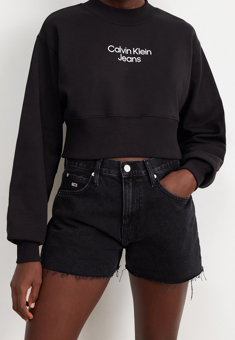 Svart kort sweatshirt med vitt "Calvin Klein Jeans"-logotyp. Matchad med svarta denimshorts med trasig kant och framfickor.