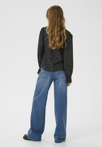 Blusa nera a pois con maniche lunghe, abbinata a jeans blu a gamba larga. La blusa presenta un tessuto morbido e una vestibilità comoda.