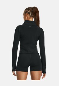 Schwarzes sportliches Langarmoberteil mit hohem Kragen, verfügt über Daumenlöcher an den Bündchen und hat eine figurbetonte Passform; kombiniert mit schwarzen Shorts.