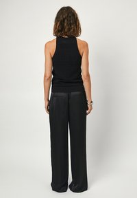 Zwarte gebreide tanktop met gestructureerde patronen, open rugontwerp en aansluitende taille. Gecombineerd met losse, hoge zwarte broek.