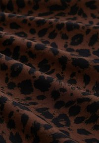 Brauner Stoff mit einem Leopardenmuster und schwarzen Flecken, der eine weiche Textur und einen glatten Fall zeigt.
