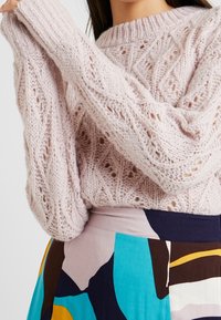 Maglione lavorato a maglia di un delicato rosa chiaro, caratterizzato da un motivo testurizzato, scollatura a costine e maniche ampie, abbinato a una gonna a fantasia colorata.