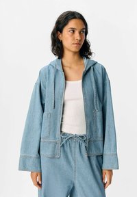 Hellblaues Jeansjackett mit Kapuze, Frontreißverschluss, zwei Taschen und Kordelzug in der Taille. Es hat eine lockere Passform und kontrastierende Nähte.