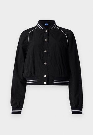 Črna bomberska jakna s skrajšanim dizajnom, ki ima bele črtaste poudarke na ovratniku in manšetah, na sprednji strani pa je zavarovana z kovinskimi gumbi.