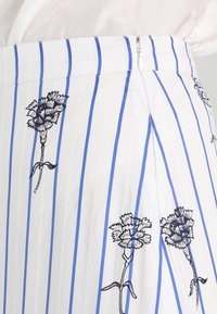 Bílá sukně s vertikálními modrými pruhy a černými květinovými potisky, s bočním zipovým zapínáním a sklady.