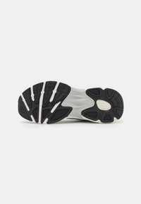 Suola di sneaker in bianco e nero con un motivo in gomma testurizzata, caratterizzato da scanalature e creste per una maggiore trazione e durabilità.