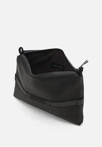 Sort lynlås pung lavet af glat materiale. Har et diskret logo og en rund form, med en pull-tab for nem åbning.