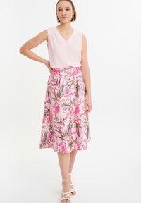 Canotta rosa chiaro senza maniche con scollatura a V accoppiata a una gonna midi floreale nei toni del rosa e del verde, caratterizzata da un design fluido e tasche laterali.