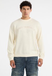 Off-white gestrickter Pullover mit gerippten Bündchen und Saum, mit "GUESS ORIGINALS" in strukturierten Stickereien auf der Brust.