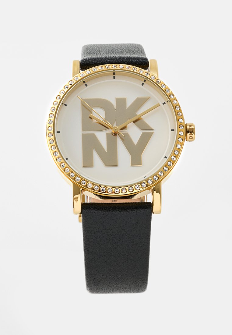 Goldfarbene Uhr mit einem runden weißen Zifferblatt, das auffällige "DKNY"-Buchstaben zeigt, einem mit Kristallen verzierten Gehäuse und einem schwarzen Lederarmband.
