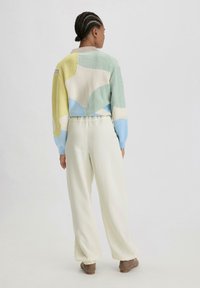 Gebreide trui in pastelkleuren met geometrische patronen; heeft een cropped ontwerp, lange mouwen en een zacht textuur. Gecombineerd met crèmekleurige broeken.