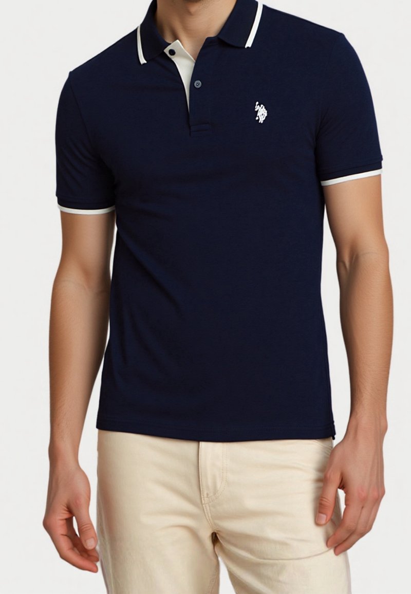 Homme portant un polo bleu marine avec un liseré blanc et un pantalon beige, présenté du cou jusqu'à mi-cuisse sur un fond uni.