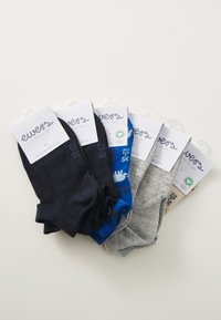 Cinco pares de calcetines de colores variados: marino, azul, gris y beige, con diferentes diseños y etiquetas con información de la marca.