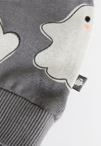 Hall halli kudumistest kampsun, millel on valged kummituse mustriga musta äärega ja virsiku värvi aktsentidega. Varrukatel soonikkoesäärised ja väike kummituse silt äärisel.