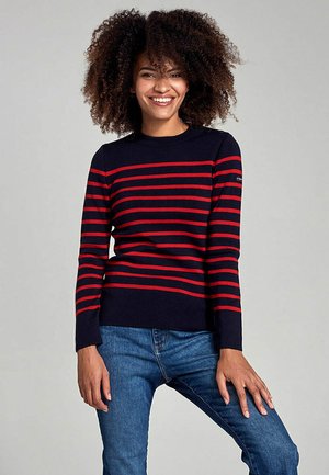 Pull marin avec des rayures horizontales rouges, col et poignets côtelés, associé à un jean bleu. Tissu doux, design décontracté, silhouette ajustée.