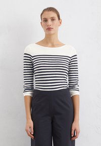 Navy and white striped long-sleeve top with a wide neckline; soft fabric; paired with dark trousers. Clean lines and moderate stretch.
