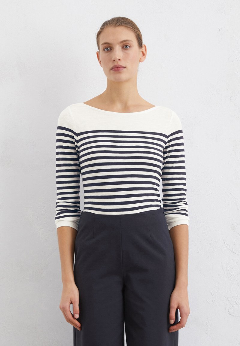 Navy and white striped long-sleeve top with a wide neckline; soft fabric; paired with dark trousers. Clean lines and moderate stretch.