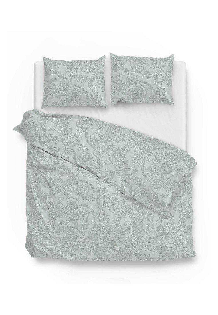 Cama doble con sábanas blancas, cubierta por un edredón azul claro y cojines con intrincados patrones florales de paisley.