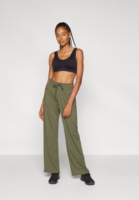 Crni crop top s širokim trakama, uparen s labavim maslinastozelenim hlačama koje imaju podesivu vezicu i bočne džepove. Crne cipele.