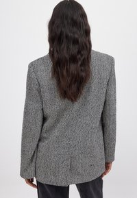 Houndstooth-kuvioitunut bleiseri harmaana ja mustana, jossa on jämäkkä muotoilu, pitkät hihat ja rento istuvuus, teksturoitu kangas.