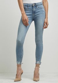 Jeans ajustados de denim azul claro con un acabado desgastado, que cuentan con una cintura alta, puños enrollados y sutiles detalles de costura.